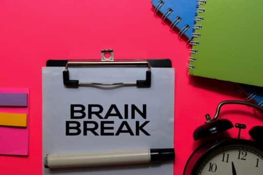 A pile of school supplies laying around a clipboard with a piece of paper that says, “brain breaks.”